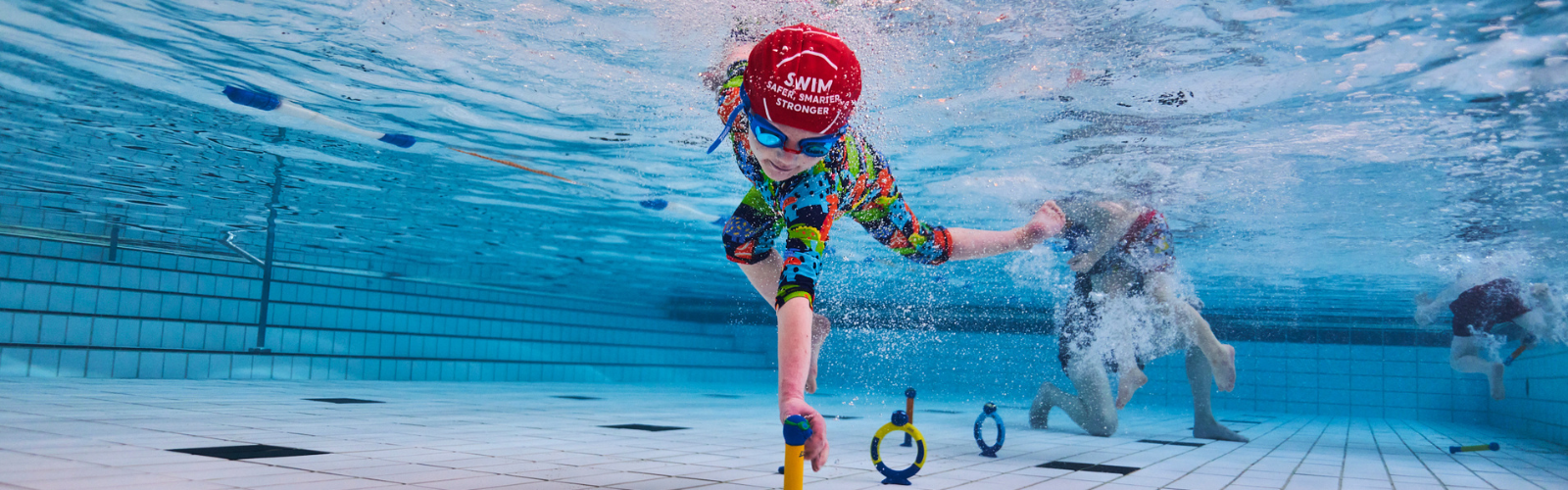 An underwater photo of a child in a swimming lesson confidently reaching for a ring toss toy