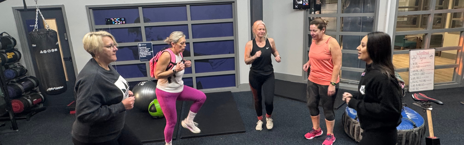 A female fitness instructor leads an energetic group of women through a high-knee exercise.